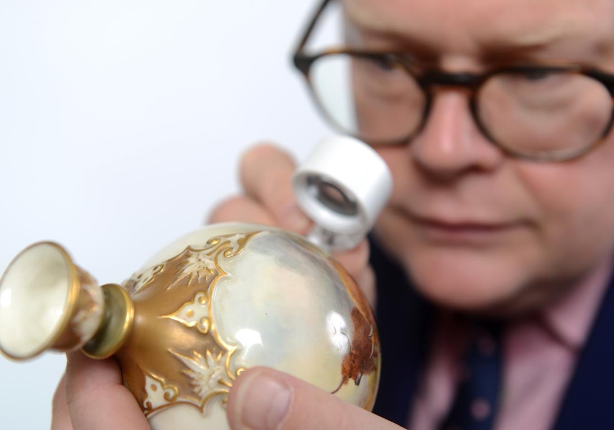 A valuer examining an object with a loupe
